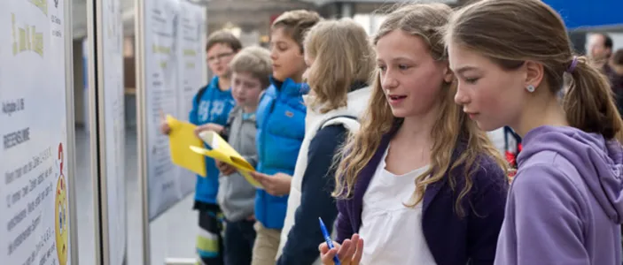 Schüler:innen stehen vor einem Poster am Tag der Mathematik